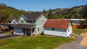 Une maison à deux étages avec un garage, une véranda et un petit abri de jardin séparé.