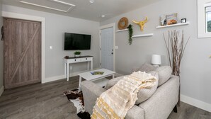 Un salon moderne avec un canapé gris, une table basse blanche, un téléviseur fixé au mur et une porte en bois.