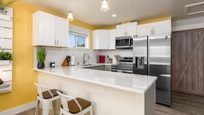 Une cuisine moderne avec des armoires blanches, des appareils en acier inoxydable et un mur d’accent jaune.