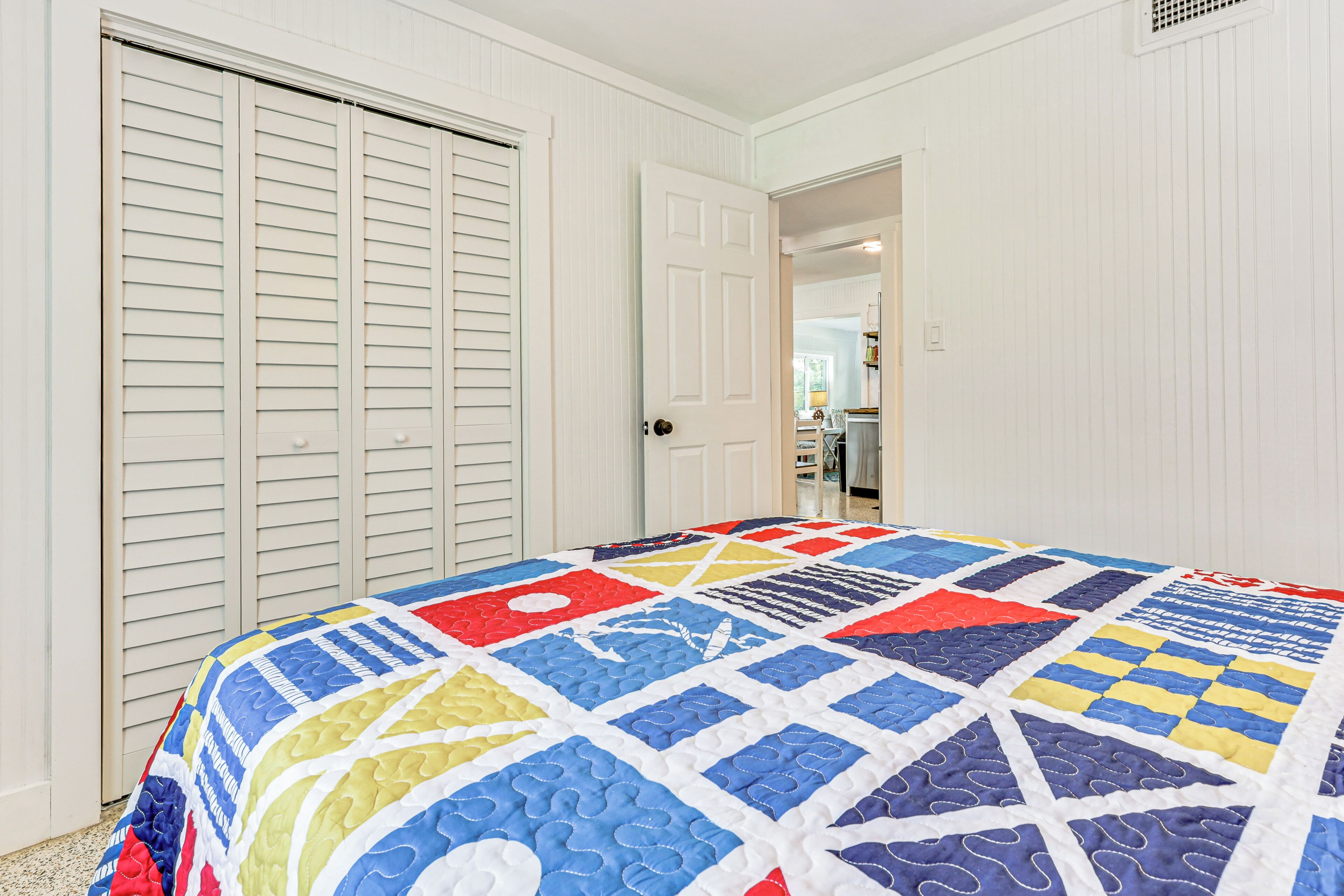 A bedroom with a colorful quilt, white walls, and a closet with sliding doors.