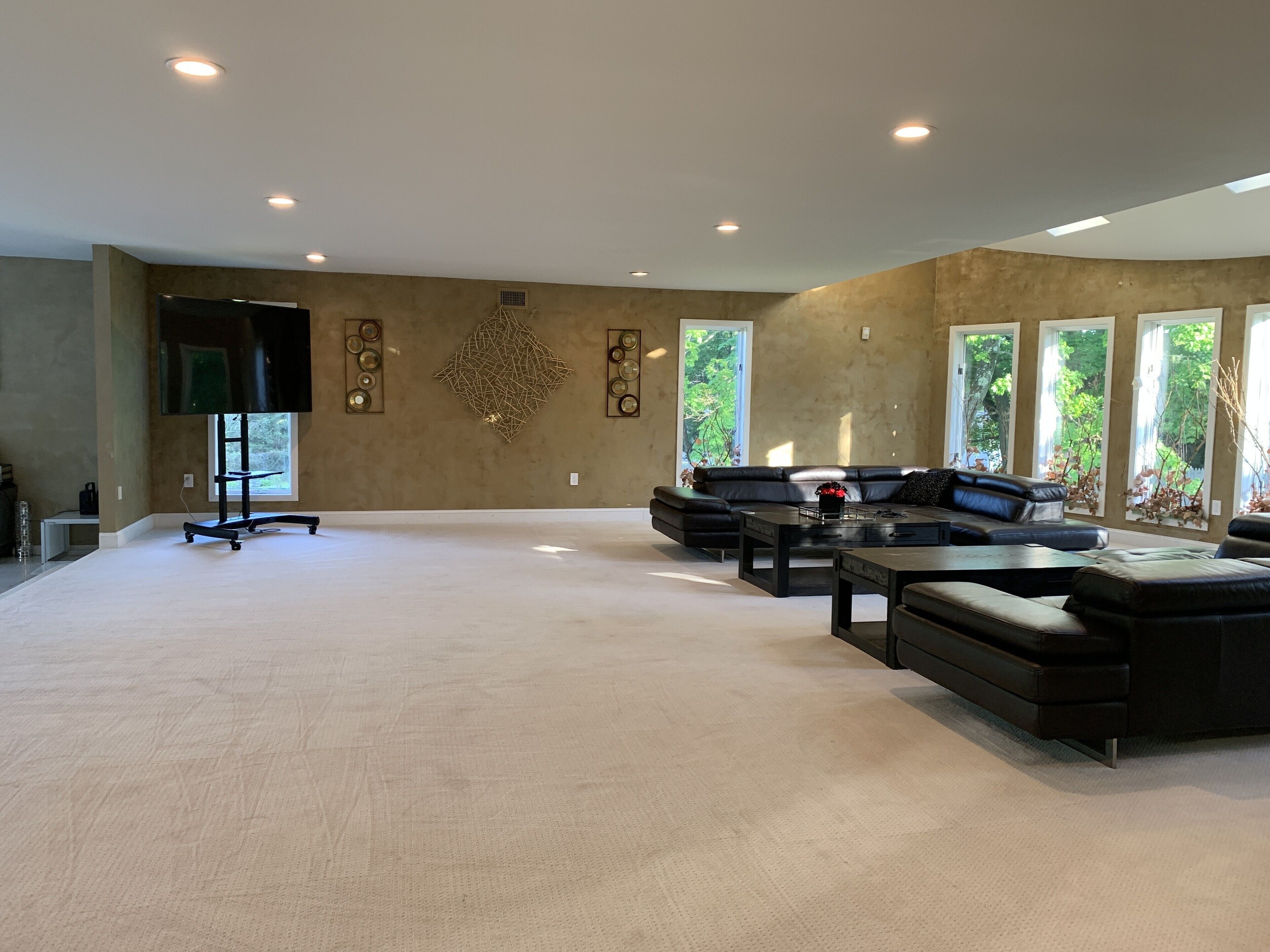 A spacious living room with a large sectional sofa, a coffee table, and a flat-screen TV mounted on the wall.