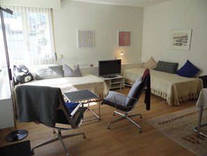 Ein Zimmer mit Bett, Schreibtisch, Stuhl, Fernseher und Kunstwerken an den Wänden.