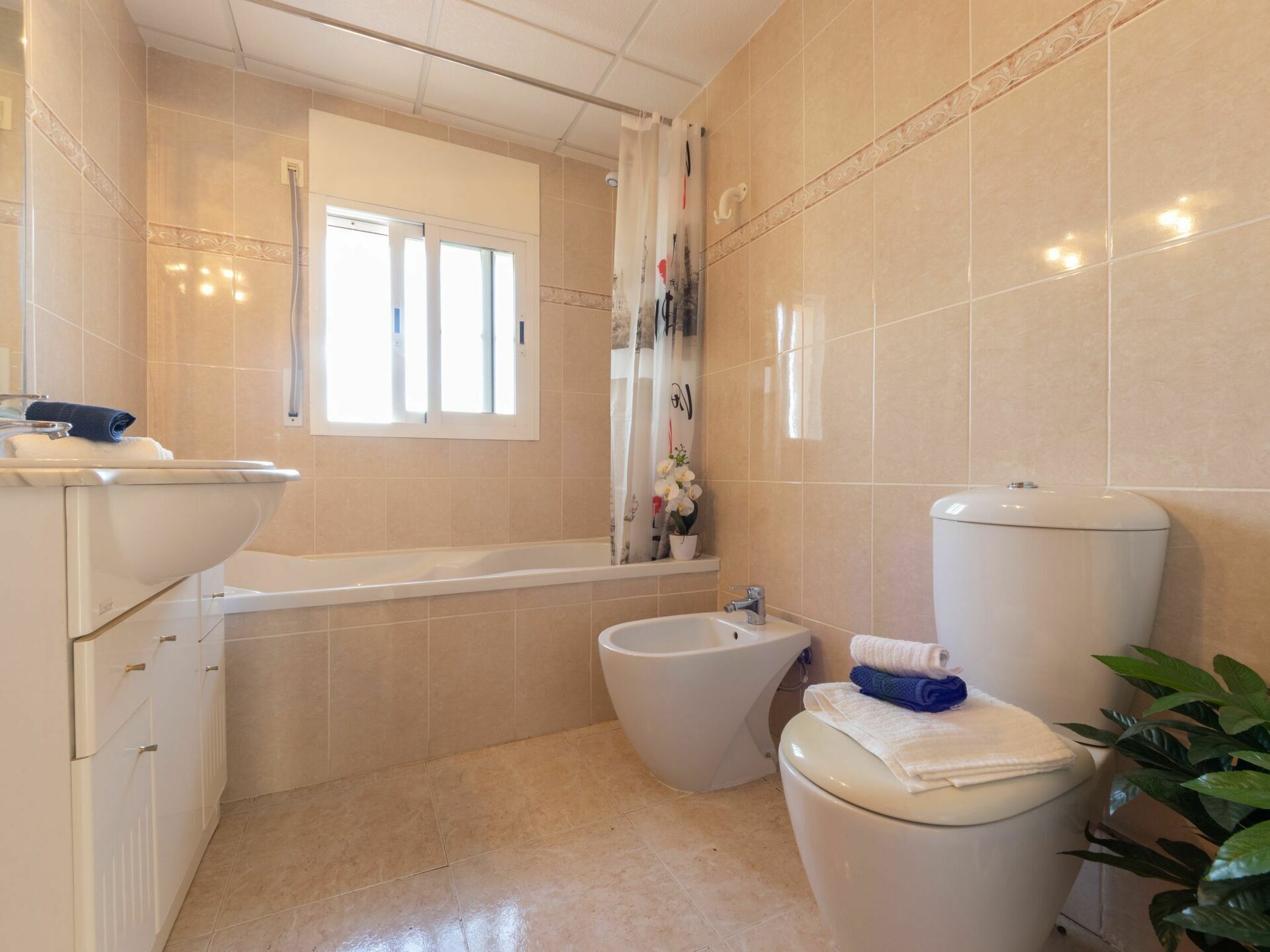 A bathroom with a toilet, bidet, bathtub, and a window.