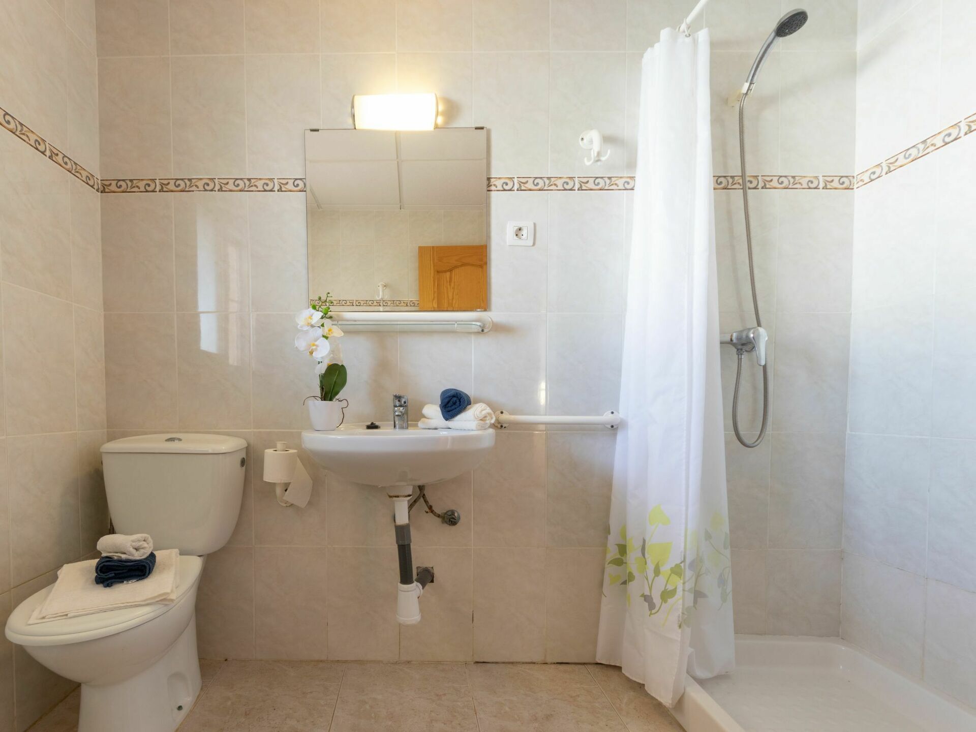 A bathroom with a toilet, sink, mirror, shower, and a towel rack.