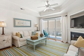 Un salon avec un canapé blanc, une table basse en bois, un tapis à rayures, un ventilateur de plafond et une cheminée.