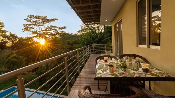 Una terraza con una mesa lista para dos personas, con vistas a una piscina y abundante vegetación.