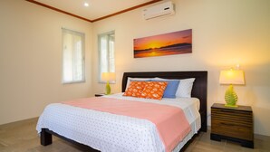 Un dormitorio con cama, dos lámparas de noche, un cuadro de un atardecer y un equipo de aire acondicionado en la pared.