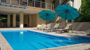Una piscina con sillones de descanso y sombrillas, un área de estar techada y un muro de piedra.