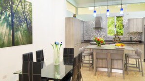 A modern kitchen with a central island, pendant lights, and a dining area with a glass table and chairs. - Parrot-dise Perch, 3BD, Heart of Manuel Antonio (Quepos)