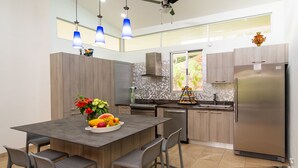 A modern kitchen with a central island, stainless steel appliances, and a large window providing natural light. - Parrot-dise Perch, 3BD, Heart of Manuel Antonio (Quepos)
