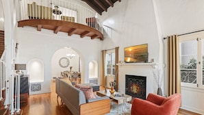 A spacious living room with a wooden staircase, a fireplace, and a large window with curtains. - LOVELY RESTORED VILLA NEAR BEVERLY HILLS (Los Angeles)