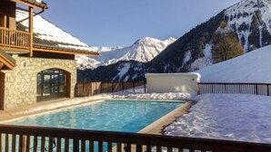 A pool area with a stone building, wooden deck, and a view of snow-covered mountains.