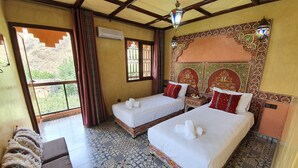 A hotel room with two beds, a large window with curtains, a patterned floor, and a decorative wall.