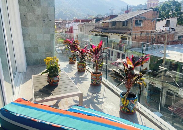 A balcony with potted plants and a colorful cushion.