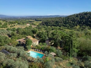 A villa with a swimming pool surrounded by lush greenery and hills in the background.