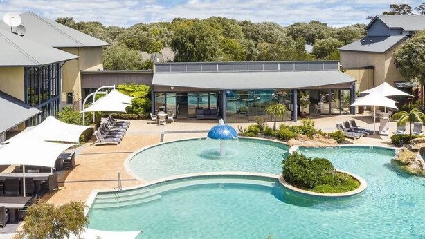 A swimming pool with lounge chairs, a covered seating area, and a building with large windows. - Baydream Believer: Lush Beachfront Resort Escape (Busselton)