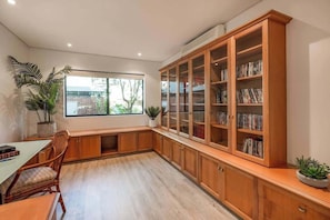 Una habitación con un armario grande de madera con puertas de vidrio, una mesa de comedor con sillas y una ventana con vistas a follaje exterior.