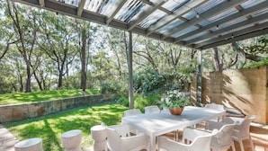 An outdoor patio with a table and chairs, surrounded by a garden and trees. - Baydream Believer: Lush Beachfront Resort Escape (Busselton)