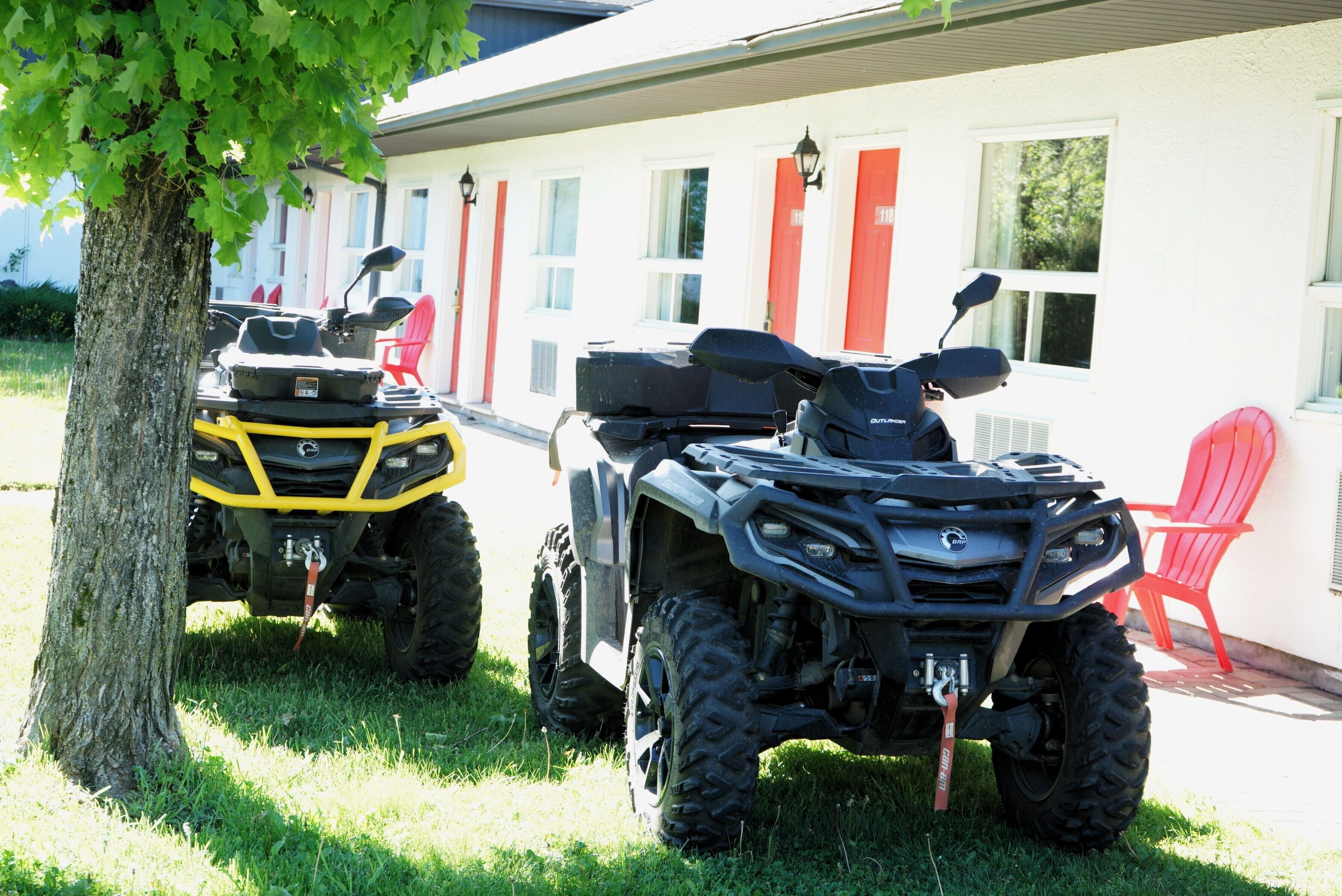 Two all-terrain vehicles parked in front of a building with red doors and windows.