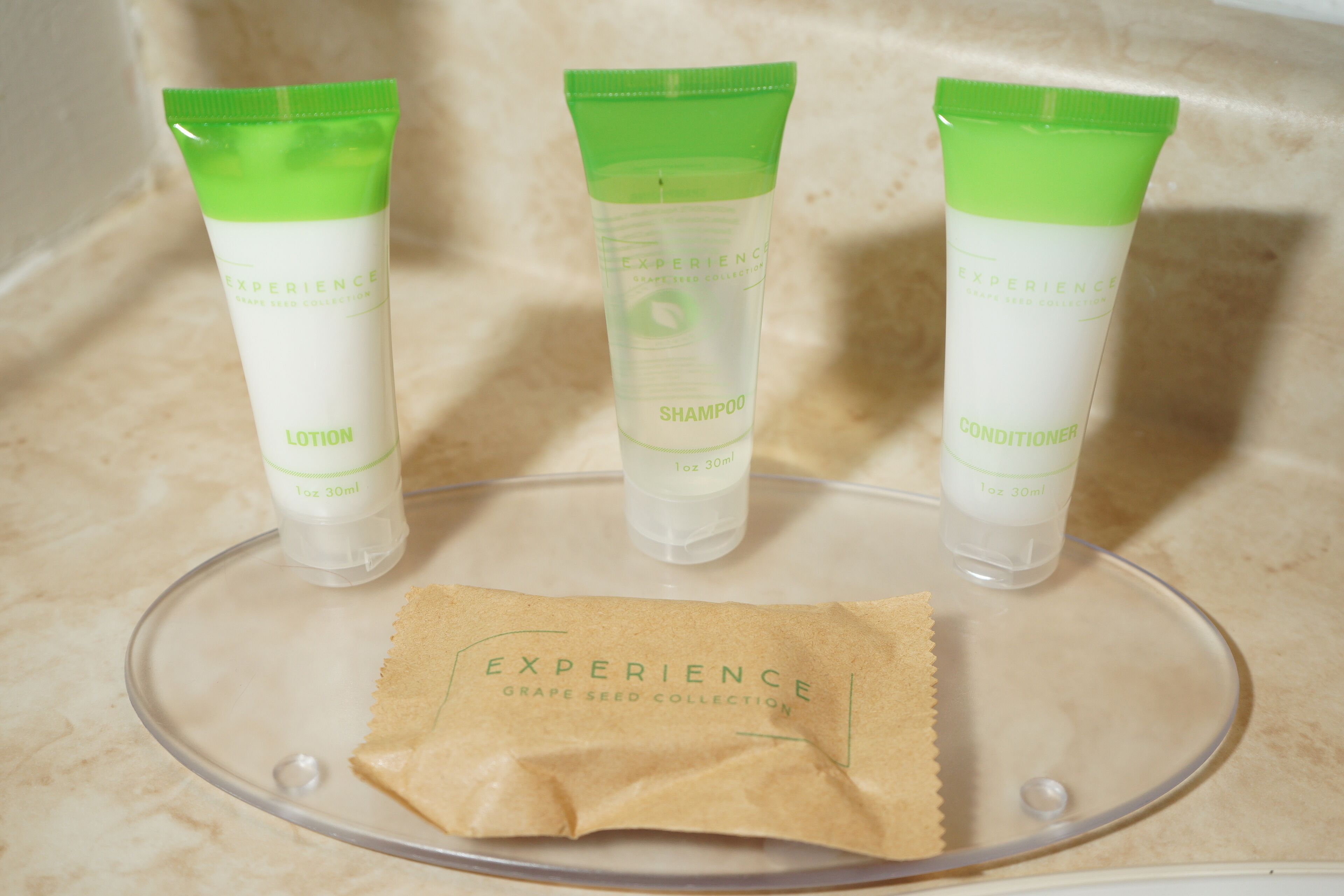 Three toiletry tubes on a clear tray with a brown paper bag labeled "EXPERIENCE GRAPE SEED COLLECTION".