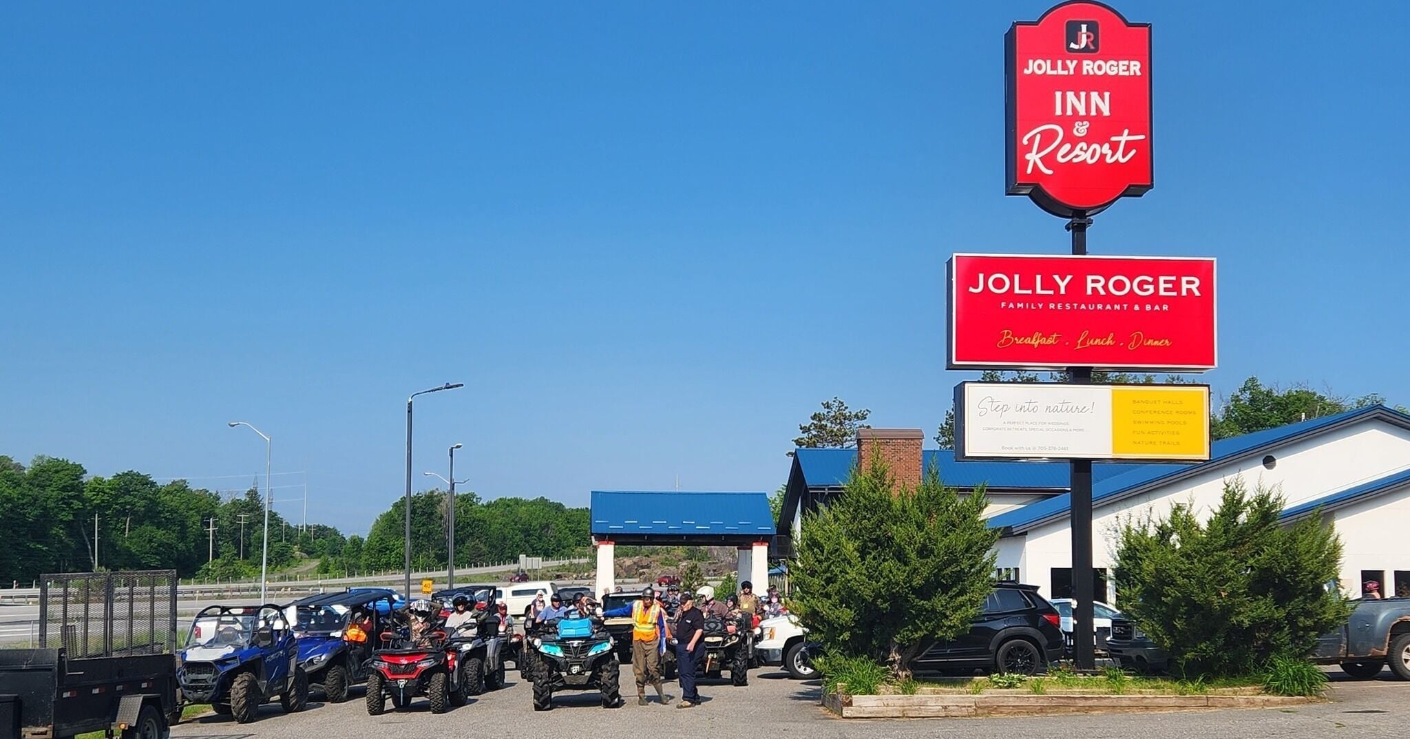 Posada y Resort Jolly Roger con un cielo azul despejado, un área de estacionamiento con vehículos todo terreno y un edificio de techo azul.