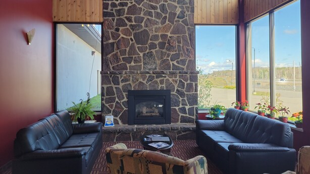 A cozy interior with a stone fireplace, leather sofas, and large windows offering a view of the outdoors. - Jolly Roger Inn & Resort (Seguin)