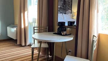 A hotel room with a round table, two chairs, a large mirror, and a window with curtains.
