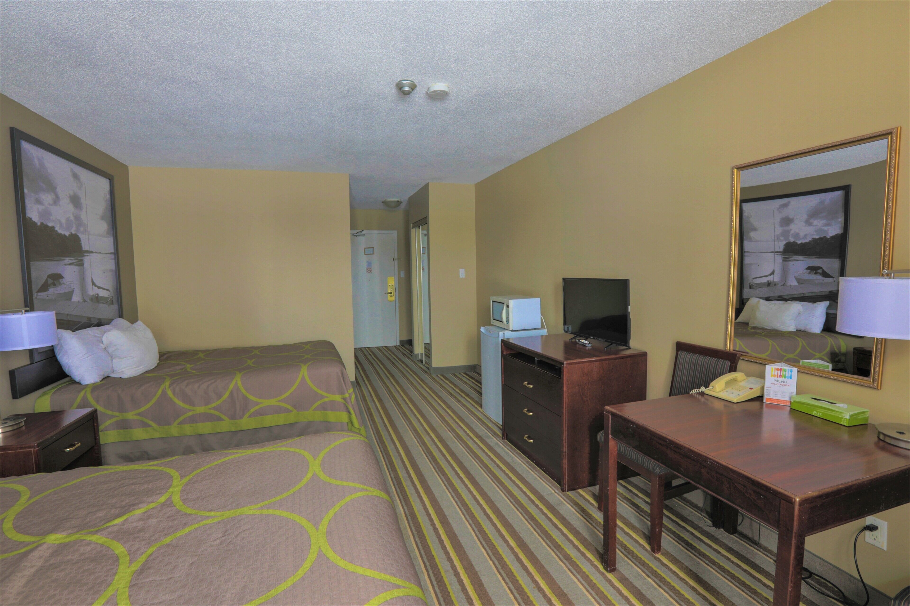 A hotel room with two beds, a desk, a chair, a television, and a mirror.