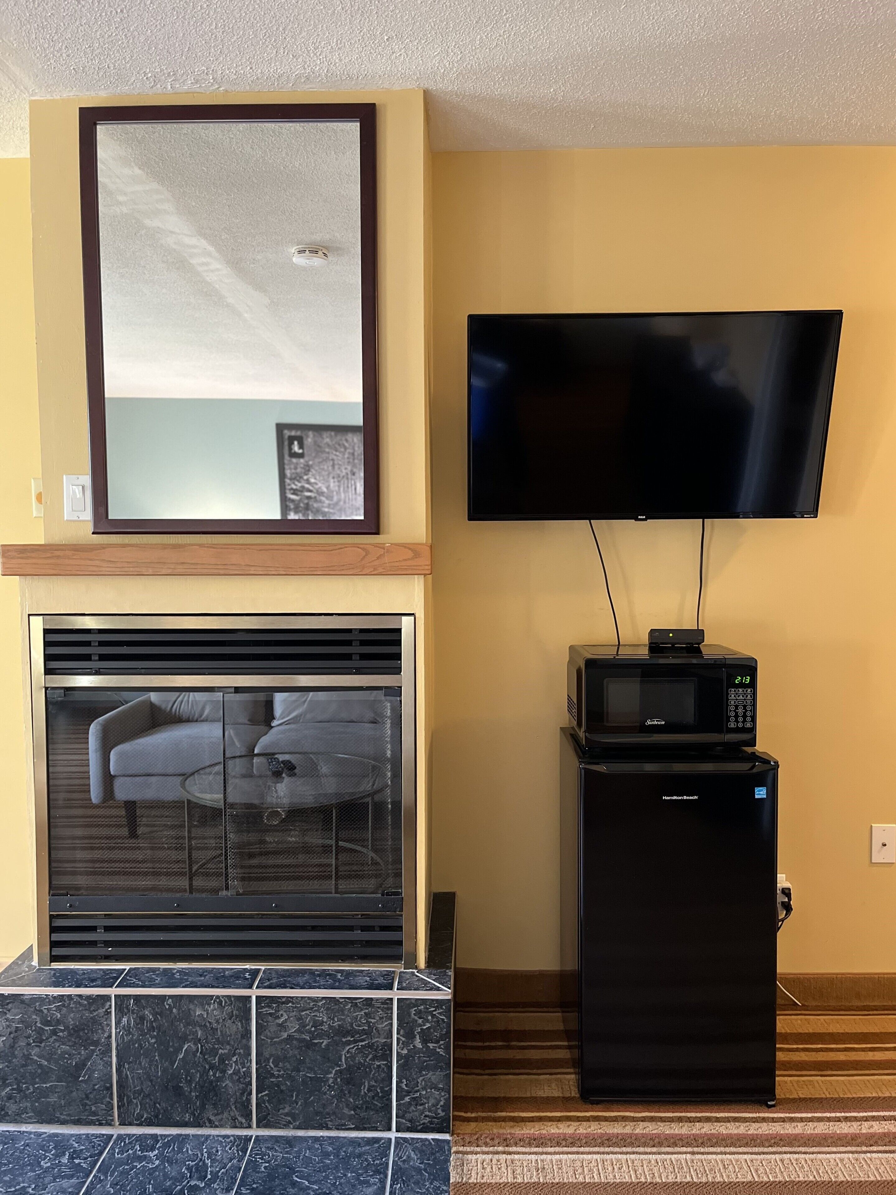 A living room with a fireplace, a flat-screen TV mounted on the wall, and a microwave on a small cabinet.