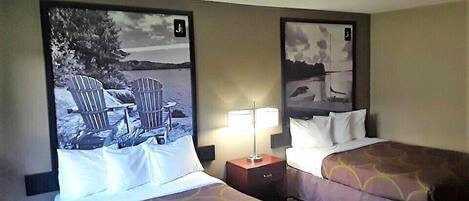 Habitación de hotel con dos camas, cada una con cabecera que representa una escena de playa. Entre las camas hay una mesita de noche con una lámpara.