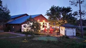 A rustic barn-style building with a blue roof, surrounded by trees and a small fenced area with string lights. - Jolly Roger Inn & Resort (Seguin)