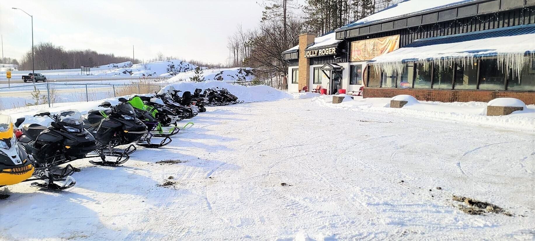 A row of snowmobiles parked in front of a building with a sign that reads "JOLLY ROGER".