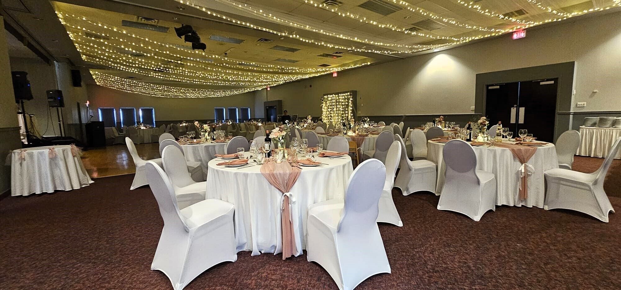 A banquet hall with round tables, white chairs, and string lights.