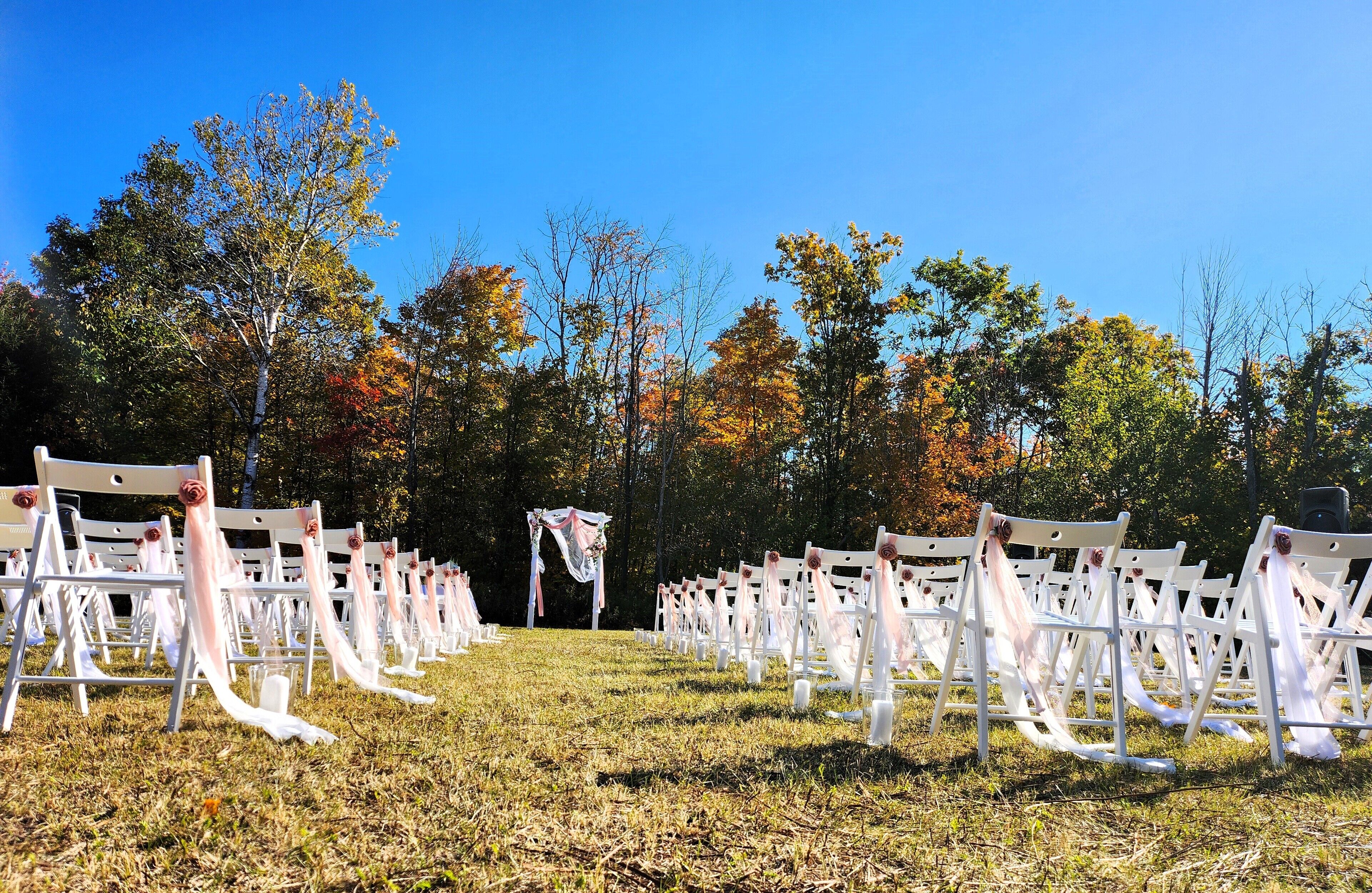 An outdoor wedding venue with rows of white chairs and a central aisle.