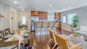 A spacious living room with a wooden dining table set for four, a large window with blinds, and a kitchen area with wooden cabinets and a refrigerator. - Walk to Disney + Brand New Pool and Rockslide + Game Room + Pet Friendly (Anaheim)