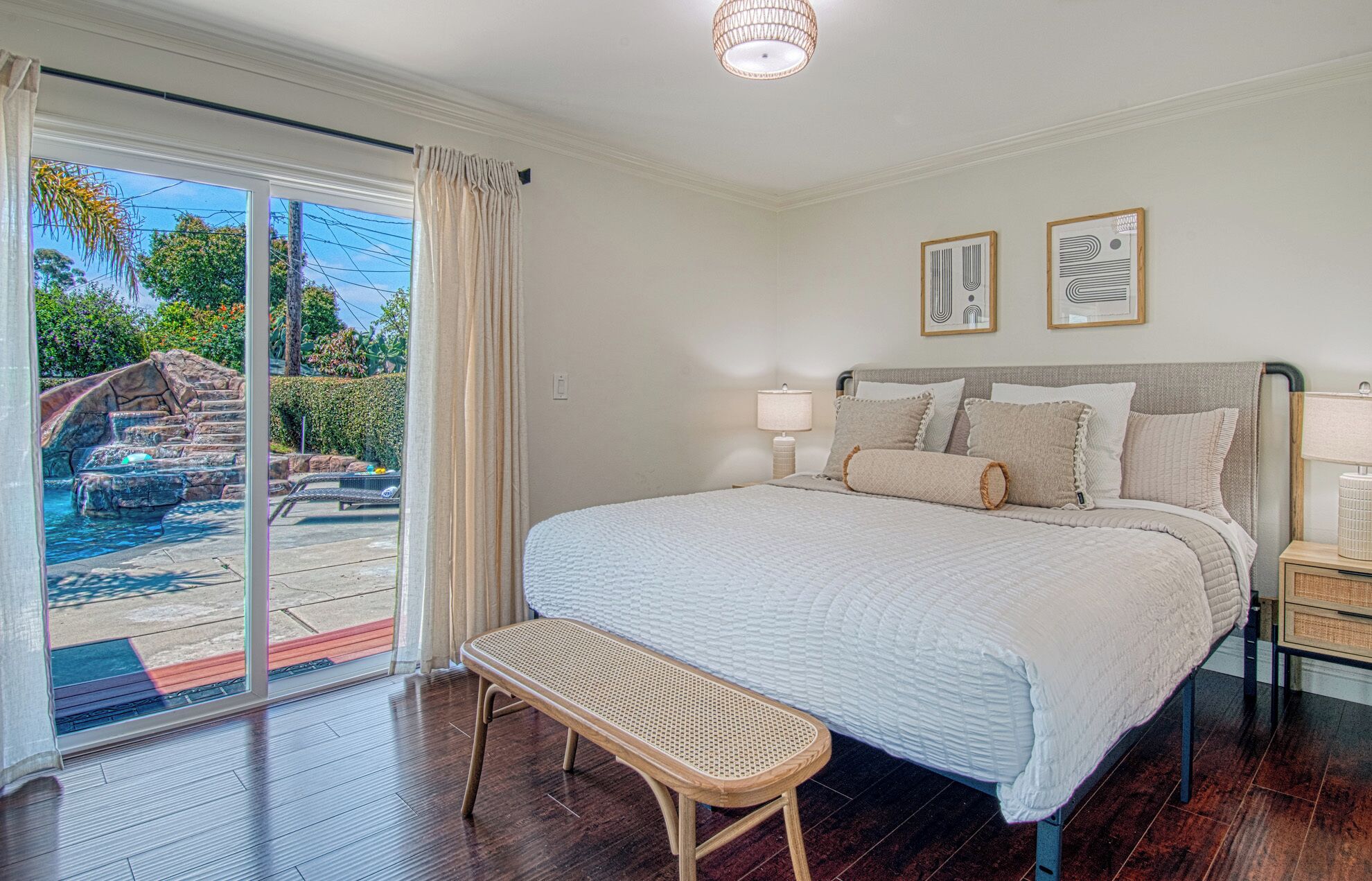 A bedroom with a bed, bench, and a view of a pool and garden.