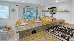 A modern kitchen with granite countertops, a gas stove, and a dining area with yellow patterned chairs. - Walk to Disney + Brand New Pool and Rockslide + Game Room + Pet Friendly (Anaheim)