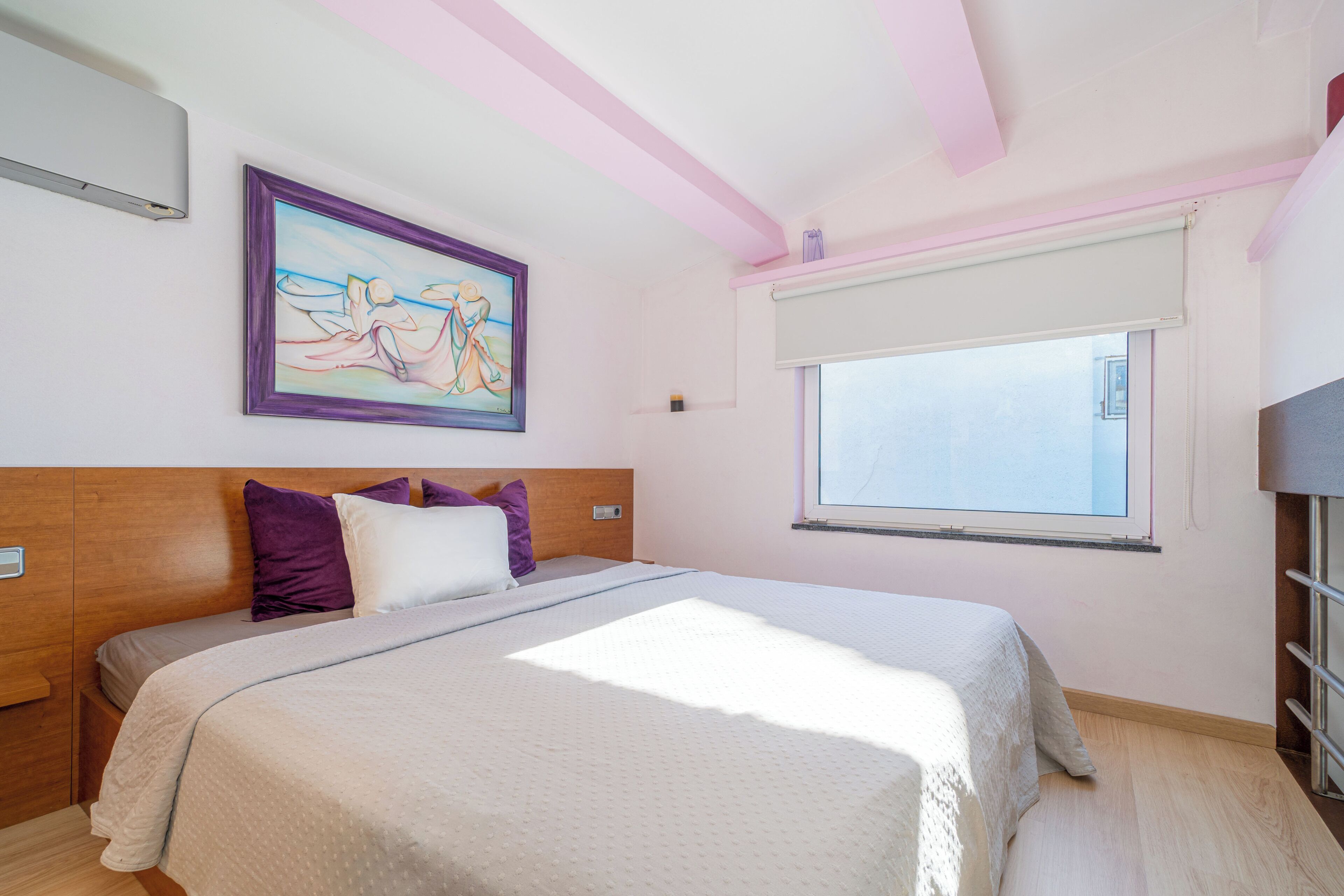 A bedroom with a bed, a window, a painting, and a wooden headboard.