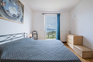 Una camera da letto con un letto, una cassettiera, un comodino, una lampada, un quadro e vista dalla finestra.