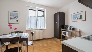 Una cocina con mesa, sillas, refrigerador, microondas y ventana con cortinas.