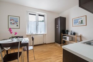 Une cuisine équipée d’une table à manger, de chaises, d’un réfrigérateur, d’un four à micro-ondes et d’une fenêtre avec des rideaux.