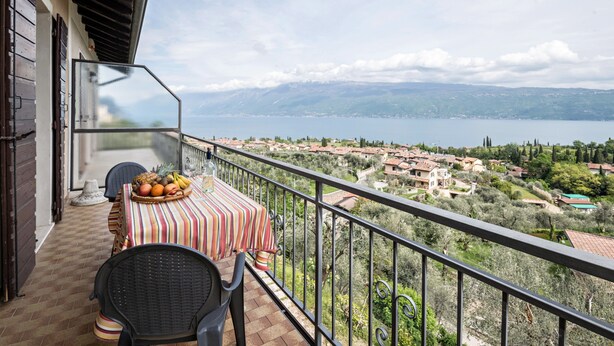 Un balcón con una mesa para dos, una silla y vistas a un lago y un pueblo.