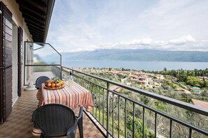 A balcony with a table set for two, a chair, and a view of a lake and town. - Holiday Apartment Al Agave Sopra with Mountain View, Lake View (Toscolano Maderno)