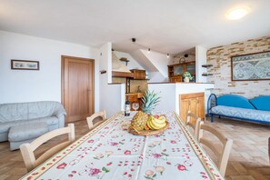 Un coin repas avec une table dressée pour deux personnes, un panier de fruits et une cuisine en arrière-plan.
