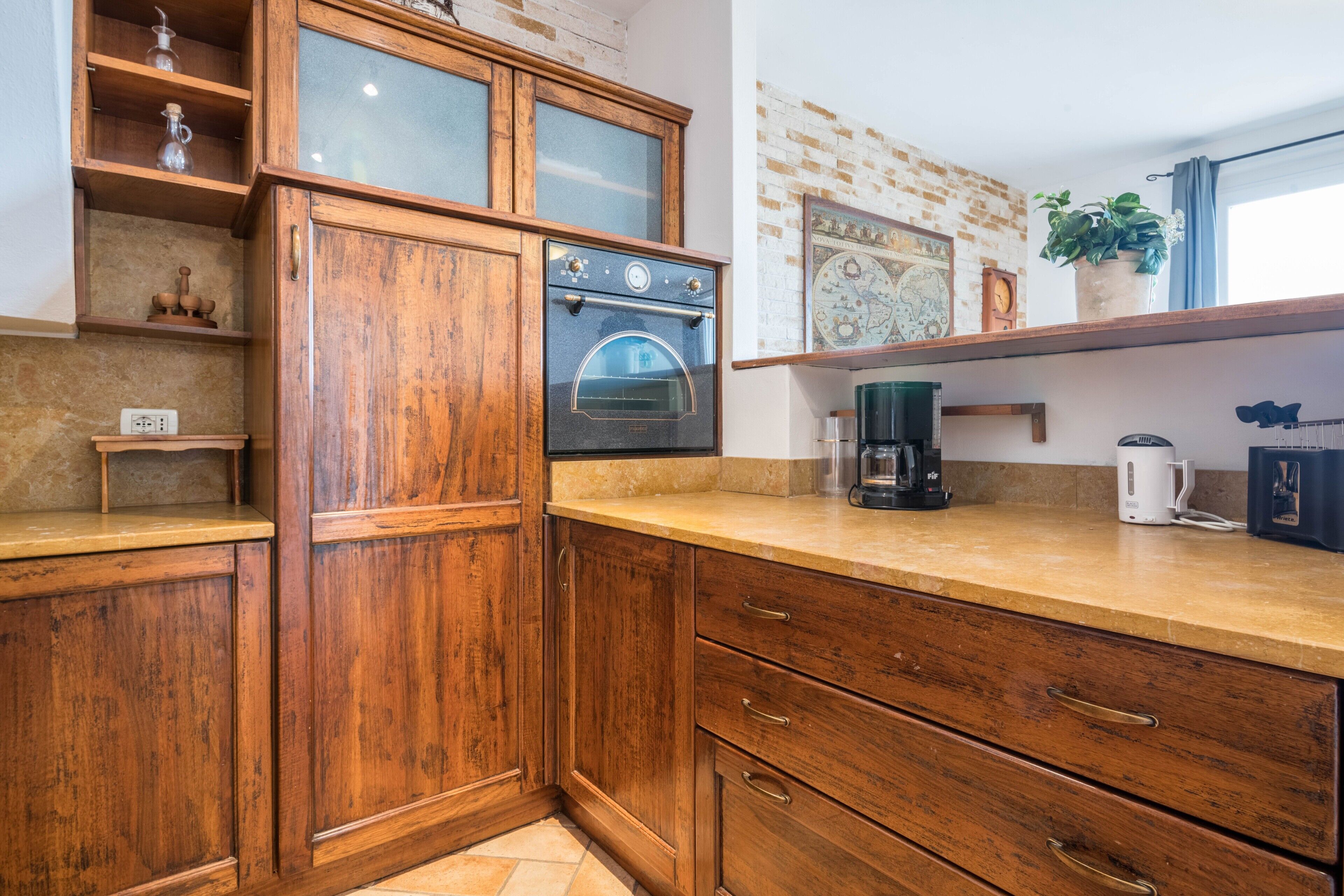 A kitchen with wooden cabinets, a built-in oven, a coffee maker, and a shelf with a potted plant.