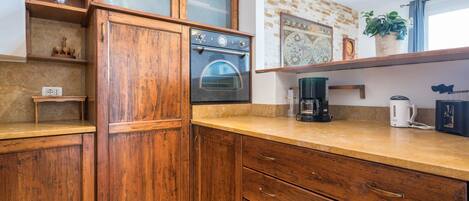 A kitchen with wooden cabinets, a built-in oven, a coffee maker, and a shelf with a potted plant.