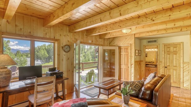 A wooden cabin interior with a dining area, a sofa, and a view of the outdoors. - Riverfront, Hot Tub, Pond, Fire Pit, Stables, Deck, Near Downtown Pagosa! (Pagosa Springs)