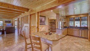 A spacious kitchen with granite countertops, wooden cabinets, and a large island with bar stools. - Riverfront, Hot Tub, Pond, Fire Pit, Stables, Deck, Near Downtown Pagosa! (Pagosa Springs)