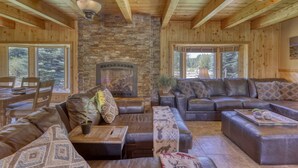 A cozy cabin interior with a stone fireplace, leather sofas, and wooden beams. - Riverfront, Hot Tub, Pond, Fire Pit, Stables, Deck, Near Downtown Pagosa! (Pagosa Springs)