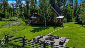 A log cabin with a deck, surrounded by a grassy area and a wooden fence. - Riverfront, Hot Tub, Pond, Fire Pit, Stables, Deck, Near Downtown Pagosa! (Pagosa Springs)